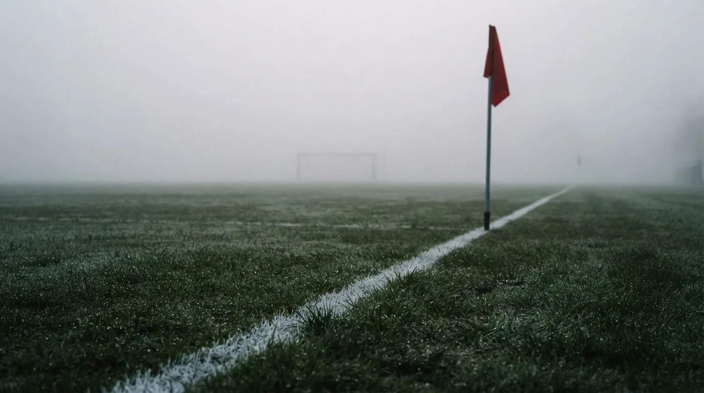 Der Rand eines Spielfelds mit weißer Linie und Eckfahne bei Nebel am frühen Morgen, ohne Menschen.