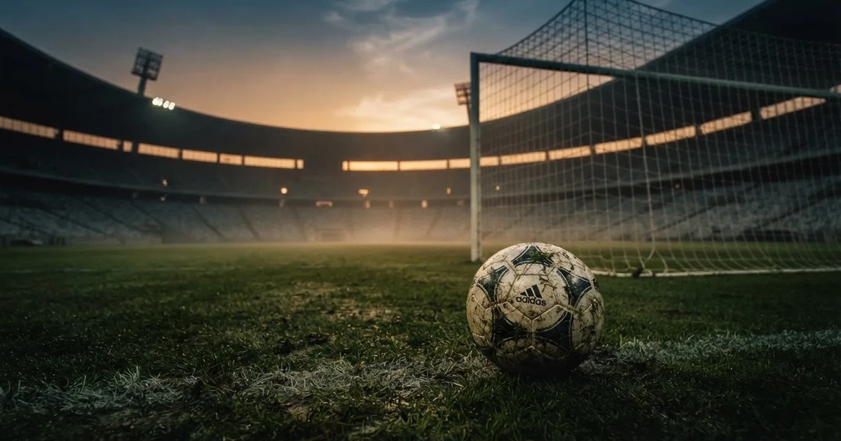 Ein Fußball liegt im Strafraum direkt vor dem Tor mit Netz, im Hintergrund leere Ränge bei Dämmerung.