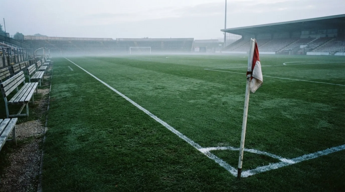 Ein Fußballplatz mit frisch gezogenen Kreidelinien im ersten Morgenlicht, leere Ersatzbänke am Spielfeldrand.