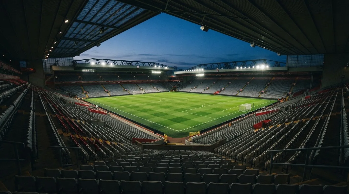 Eine leere Stadiontribüne unter Flutlicht aus der Ferne betrachtet, die Rasenfläche leuchtet grün in der Dämmerung.