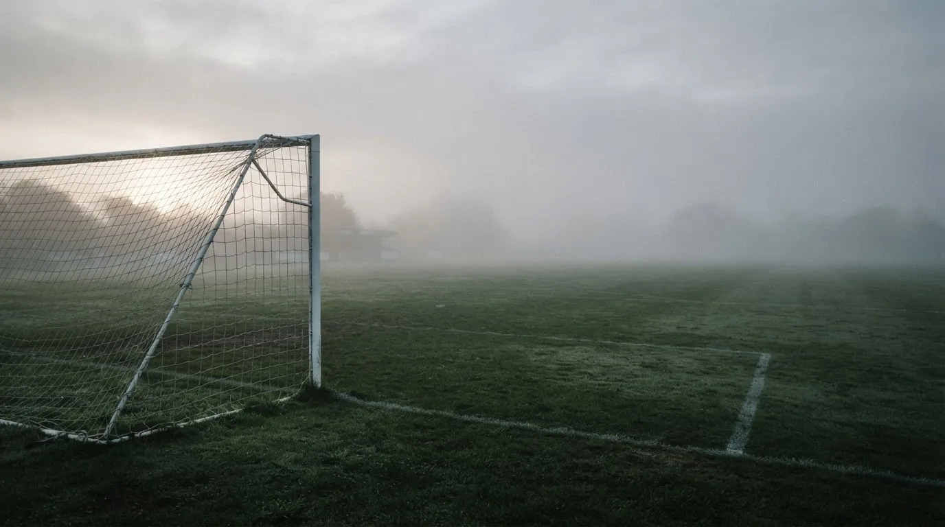 Ein Fußballtor mit Netz im Morgennebel auf einem leeren Platz, die Linien nur schwach zu erkennen.