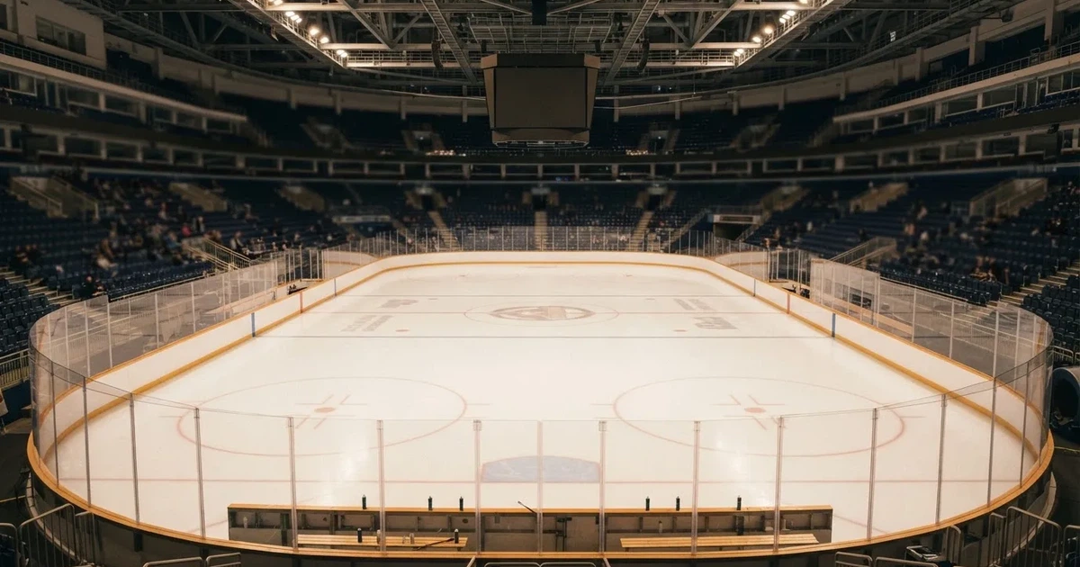 Eine Eishockeyhalle von der Tribüne aus gesehen, spiegelglatte Eisfläche, Banden ohne Schriftzüge, helles Flutlicht.