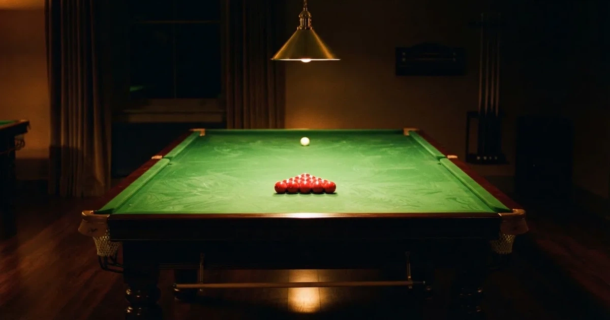 Ein Snookertisch mit grünem Tuch und aufgebauten roten Kugeln in einem abgedunkelten Raum unter einer hängenden Lampe.
