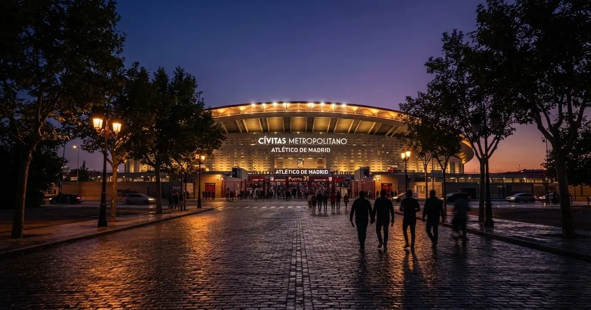 Ein großes Fußballstadion mit hell erleuchtetem Rund, aus der Ferne am Abend gesehen, davor eine breite Allee mit Laternen.
